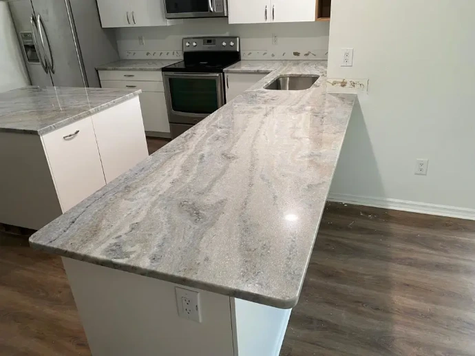 Kitchen countertop installation with gray stone-look surface, extended breakfast bar, undermount sink cutout, white cabinetry, stainless steel appliances, and wood-look flooring