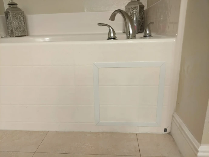 Bathtub access panel installation with clean trim, white tile surround, Roman tub faucet, and finished bathroom wall detail for easy maintenance access.