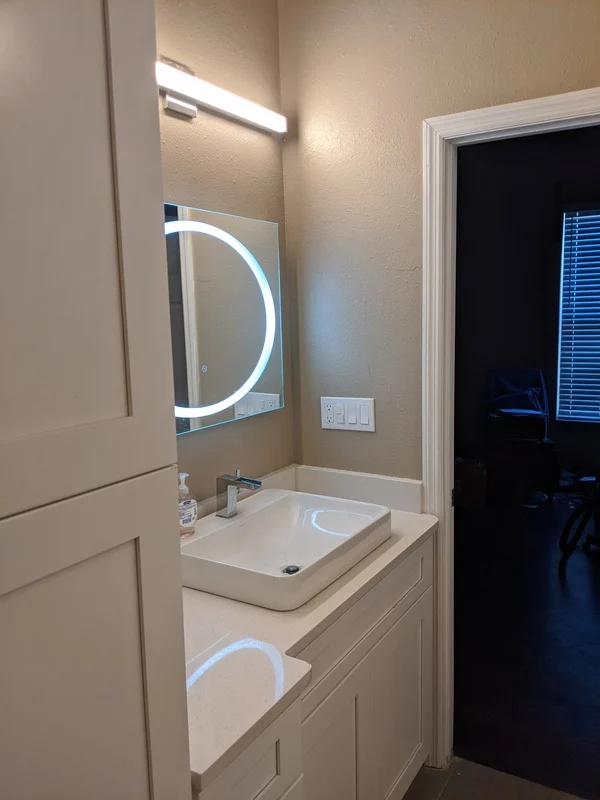 Bathroom vanity installation with white shaker cabinet, vessel sink, modern faucet, LED mirror, wall lighting, and clean trim details for a bright bathroom upgrade.