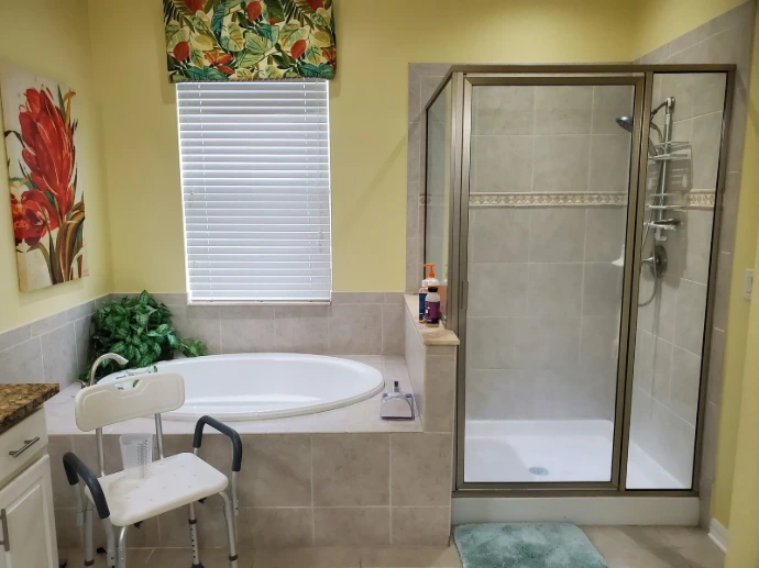 Accessible bathroom with walk-in shower, built-in tub, tile surround, handheld shower fixture, safety shower chair, natural light, and practical layout for comfortable everyday use.