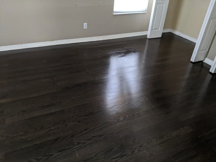 Dark wood flooring installation in an empty room with a glossy finished surface, clean baseboard edges, and a smooth upgraded look for a refreshed interior space.