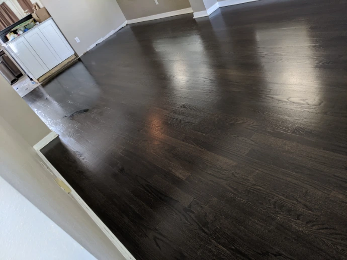 Dark wood flooring installation with smooth finished surface, rich stain color, clean baseboard edges, and open interior layout for a polished home upgrade.
